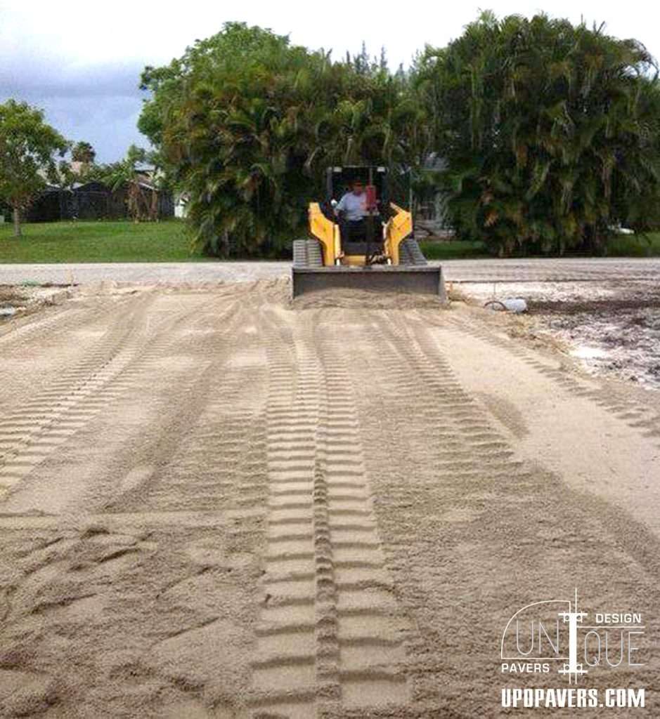 Skid steer leveling sandy ground for paving projects in landscaped area.