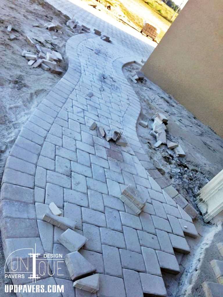 Curved stone pathway installation with scattered bricks on sandy ground.