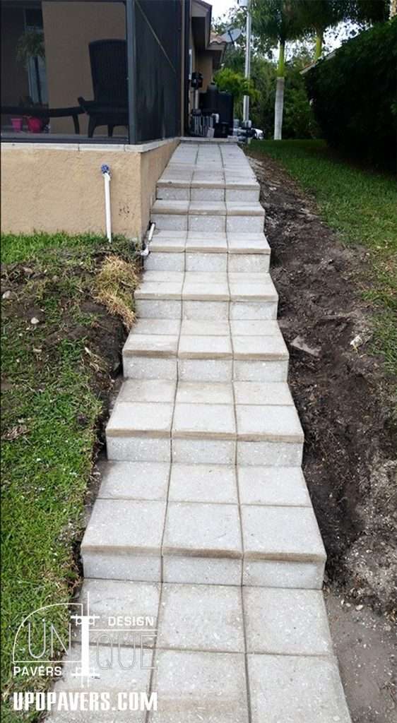 Paved walkway leading to a house, featuring rectangular concrete stones and grass edges.