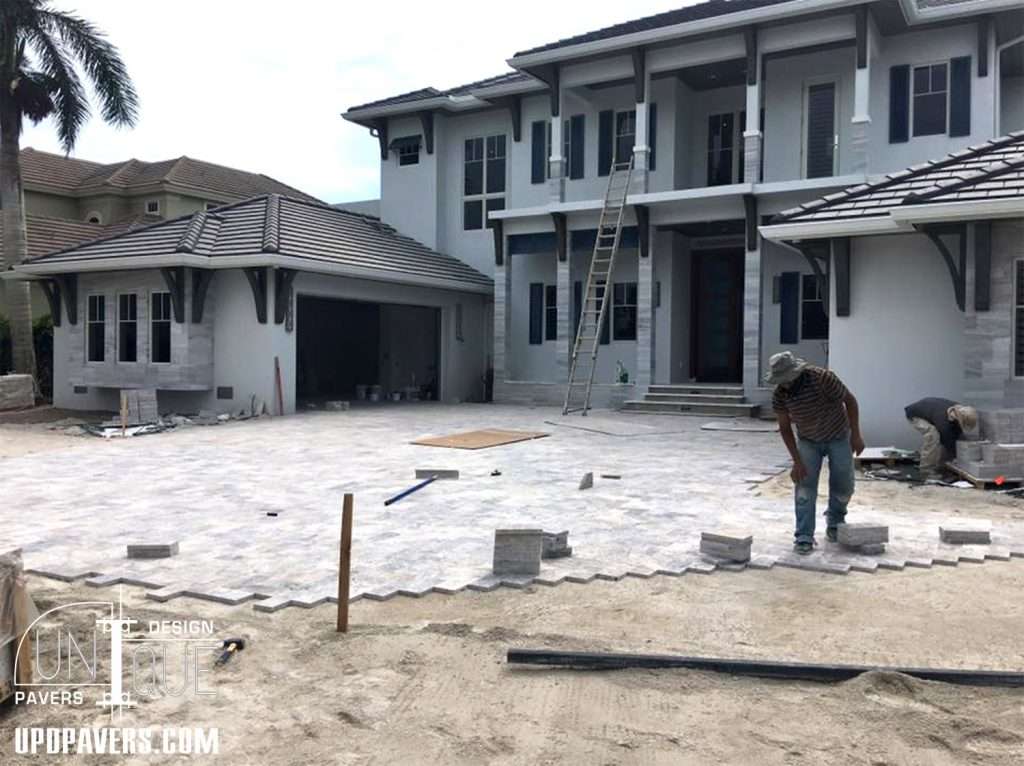 Paver installation at a modern home with workers laying stone in a landscaped area.