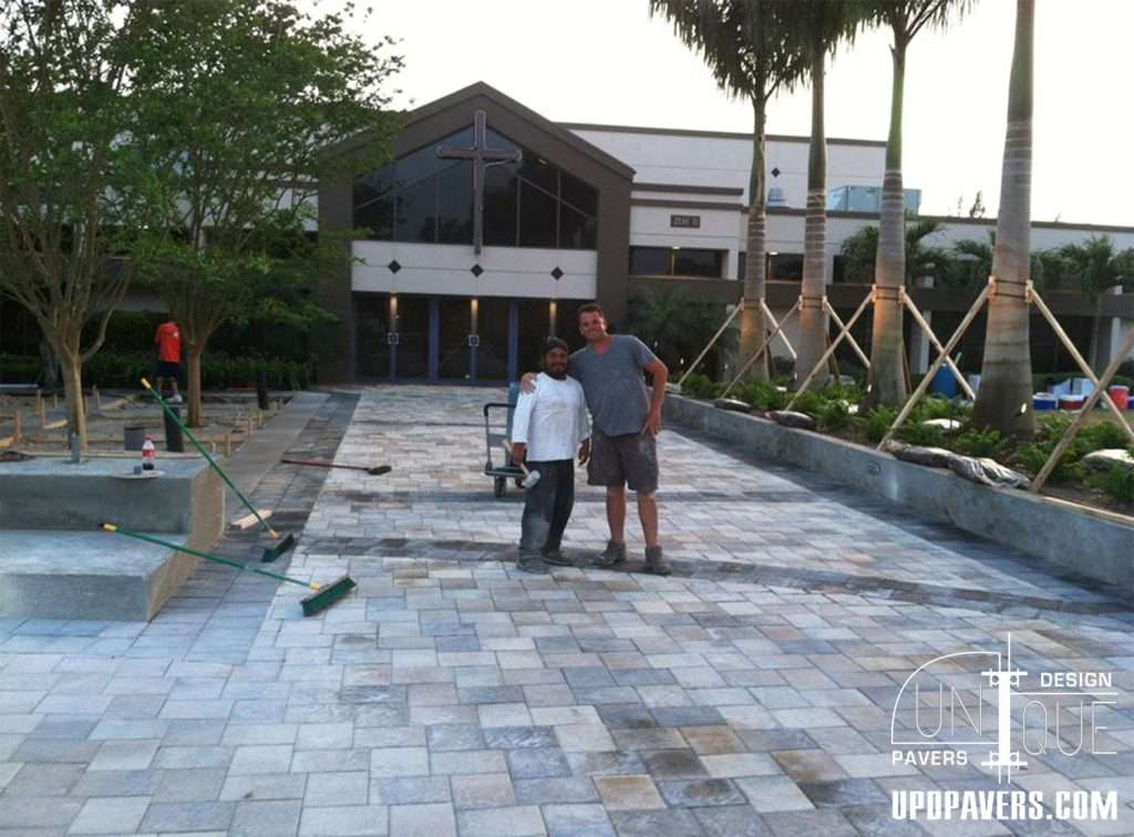 Workers posing on a newly paved outdoor area with pavers and landscaping.