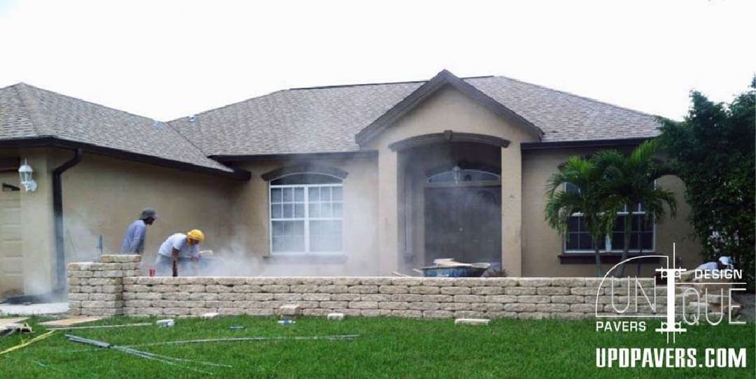 Workers installing pavers in front of a house with lush green grass and landscaping.