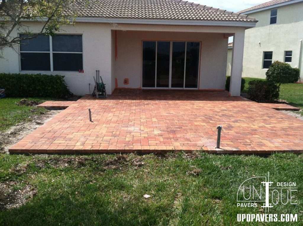 Newly installed brick paver patio behind a house, ready for outdoor use, with landscaping.