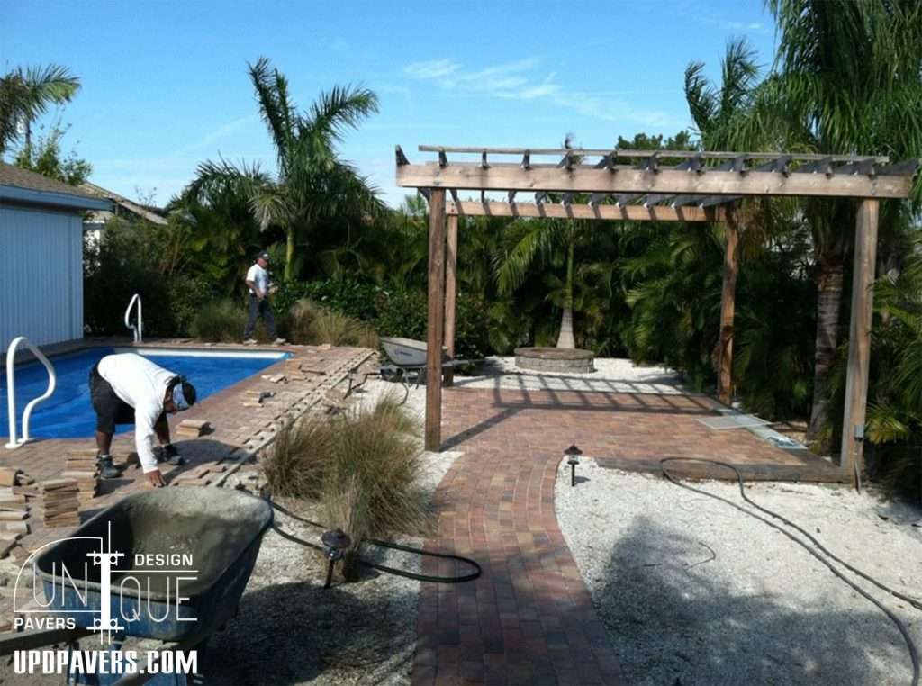 Paver installation around a pool and pergola in a tropical backyard setting.