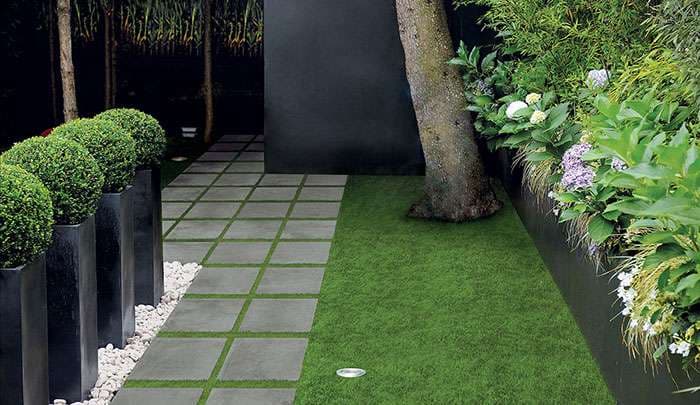 Modern garden design featuring stone walkway, lush grass, and decorative shrubs in planters.