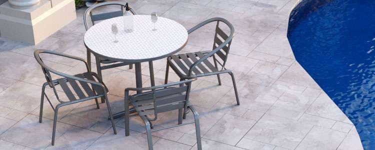 Outdoor patio dining set with a round table and four chairs by a swimming pool.