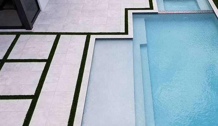 Modern pool and patio design featuring tile flooring and artificial grass accents.