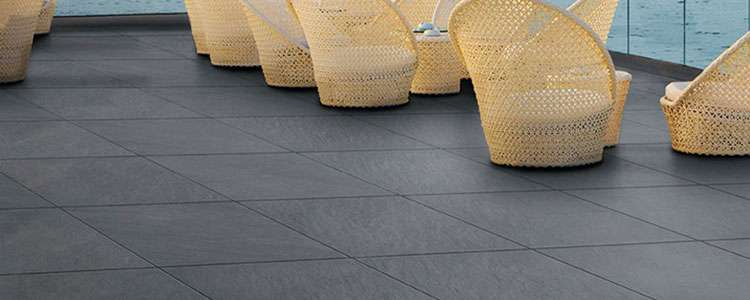 Elegant outdoor seating area with woven chairs on a modern stone patio by the water.