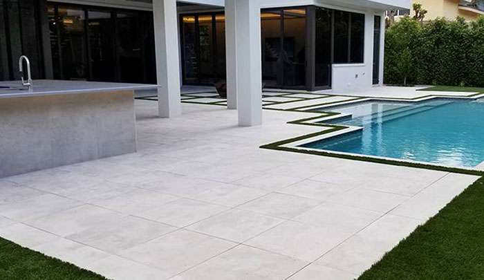 Modern outdoor patio with sleek tiles, a pool, and landscaped greenery. Ideal for home improvement.
