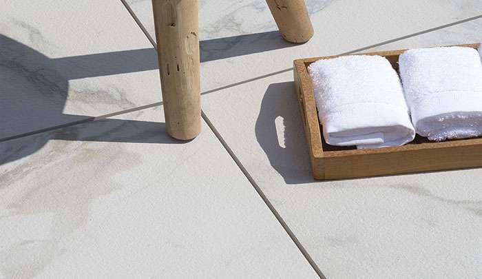 Wooden stool next to a tray of white towels on a tiled floor.