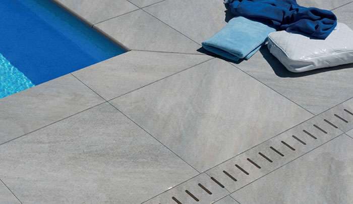 Modern gray poolside tiles with towels beside a blue pool.