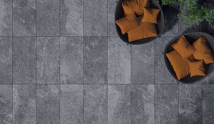 Modern outdoor patio with gray stone tiles and two chairs with orange cushions.