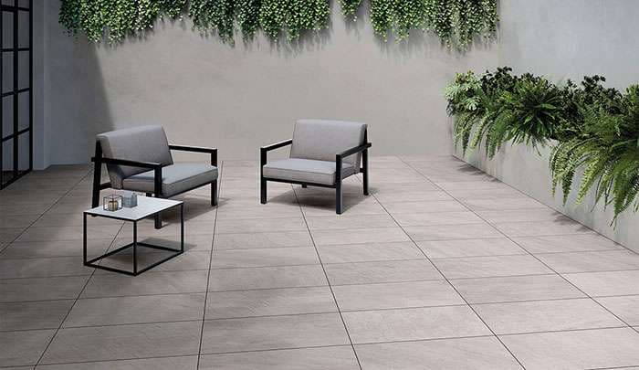 Modern patio featuring gray chairs, a sleek table, and lush greenery along the wall.
