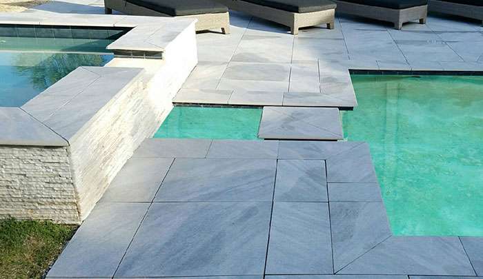 Modern stone patio surrounding a pool with clear blue water and stylish loungers.