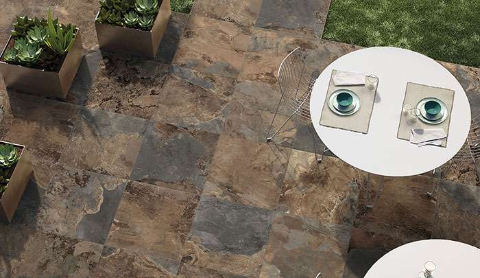 Outdoor dining area with modern tables, plates, and stone tile flooring surrounded by planters.