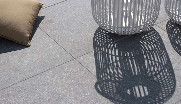 Gray tiled floor with white woven baskets casting intricate shadows beside a beige pillow.