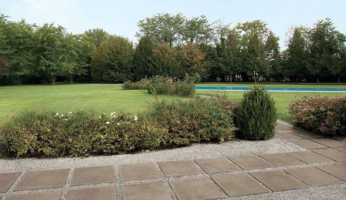 Lush green garden with a pathway, shrubs, and a pool in the background.