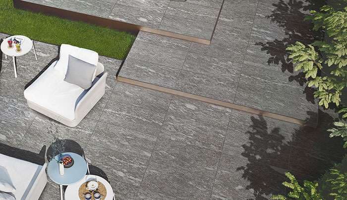 Modern outdoor patio with gray stone tiles, stylish seating, and greenery for a relaxing ambiance.