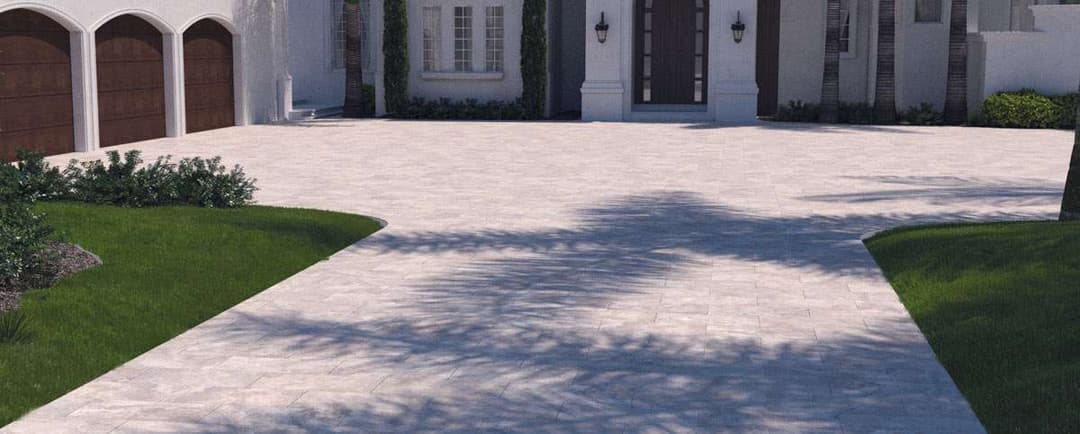 Elegant driveway with paver stones leading to a luxurious home surrounded by lush greenery.