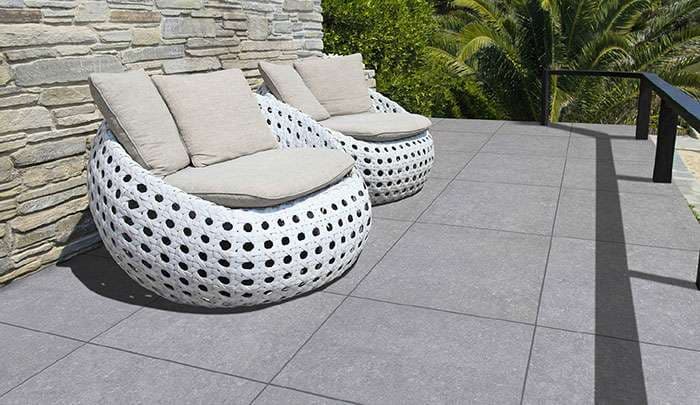 Modern outdoor patio with stylish white lounge chairs and grey stone flooring.