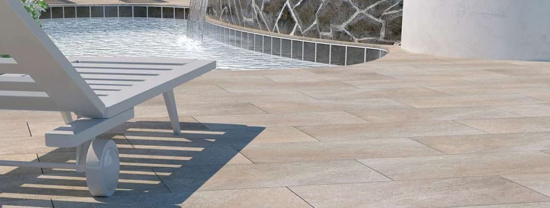 Lounge chair by a pool with water feature and stone wall, highlighting outdoor relaxation.