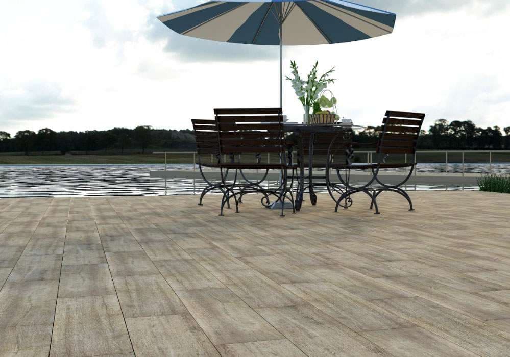 Outdoor patio with a table, chairs, and umbrella by the water, featuring wood-like flooring.