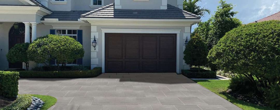 Modern home exterior with a landscaped yard and a paved driveway leading to a wooden garage door.