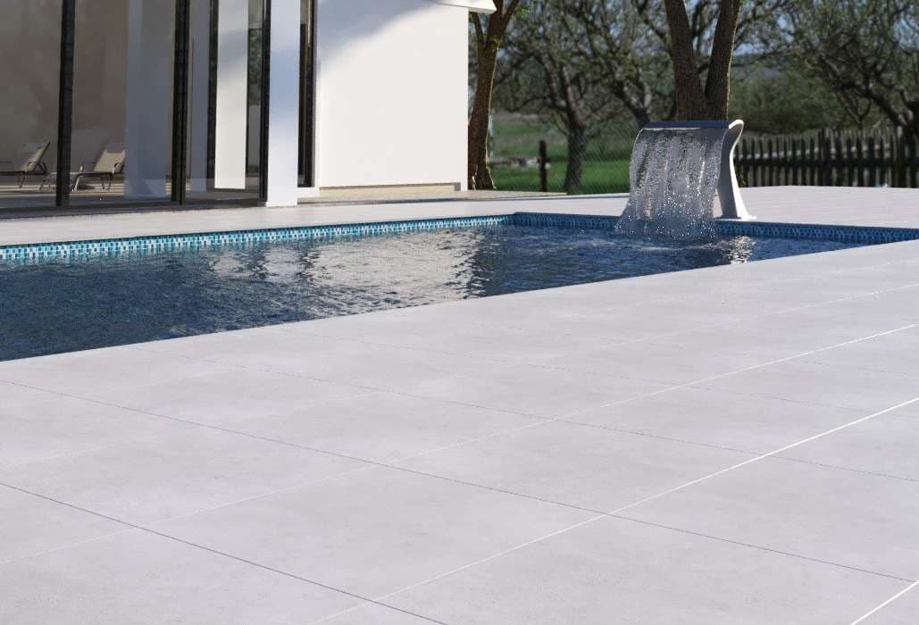 Modern poolside with white tiles and a water feature, surrounded by greenery.