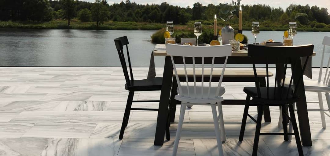 Outdoor dining setup with black and white chairs by a scenic lake view. Elegant table setting.