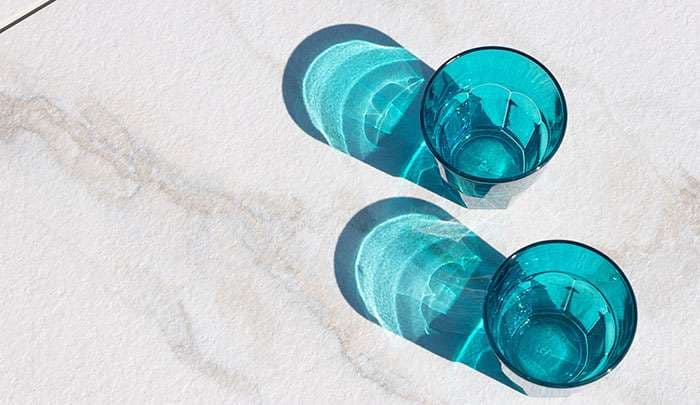 Two turquoise glasses casting shadows on a light marble surface.