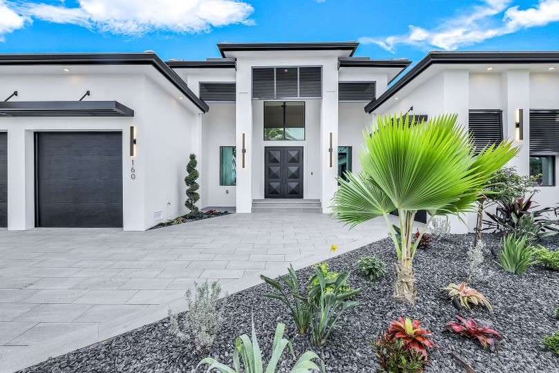 Modern luxury home exterior with landscaped front garden and palm tree in sunlight.