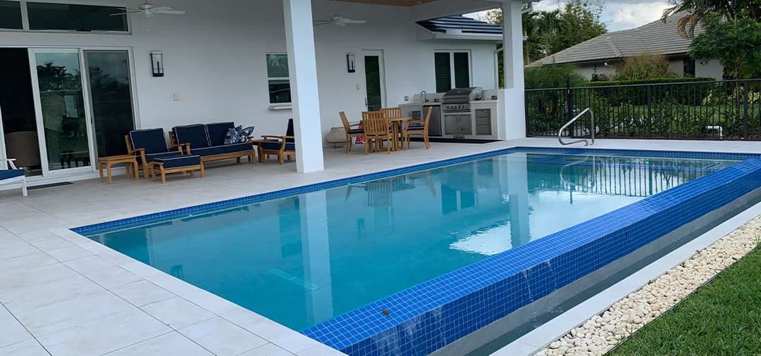 Modern backyard with a pool, lounge chairs, and outdoor dining area, surrounded by greenery.