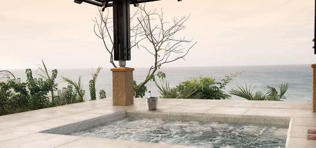 Luxurious outdoor hot tub with ocean view and tropical vegetation. Perfect for relaxation.