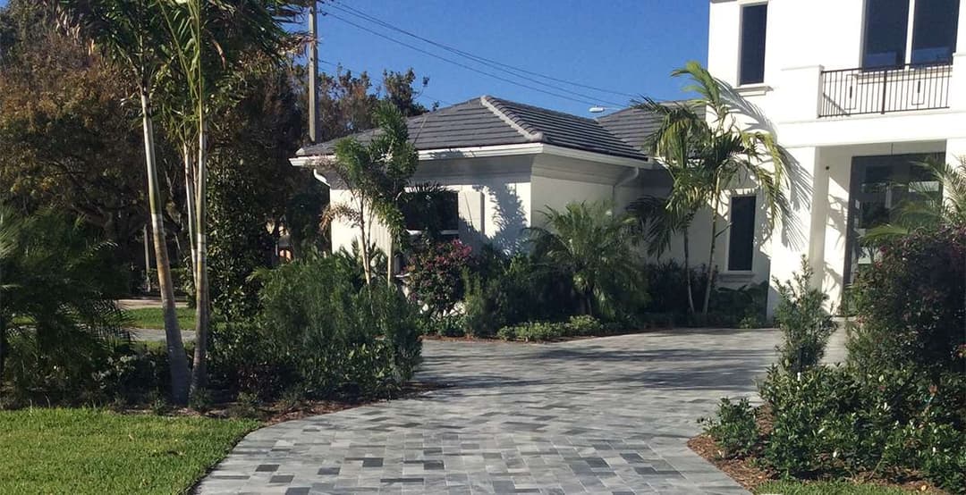 Modern home with landscaped garden and paver driveway under blue sky.