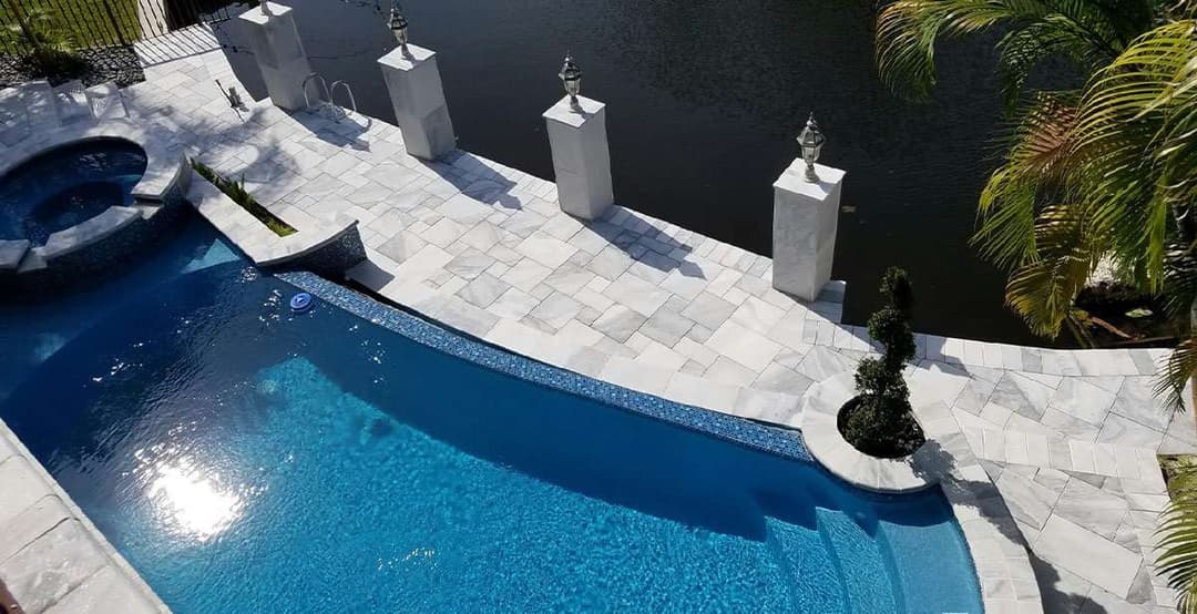Luxury swimming pool with spa and landscaped patio by water, featuring modern stone tiles.