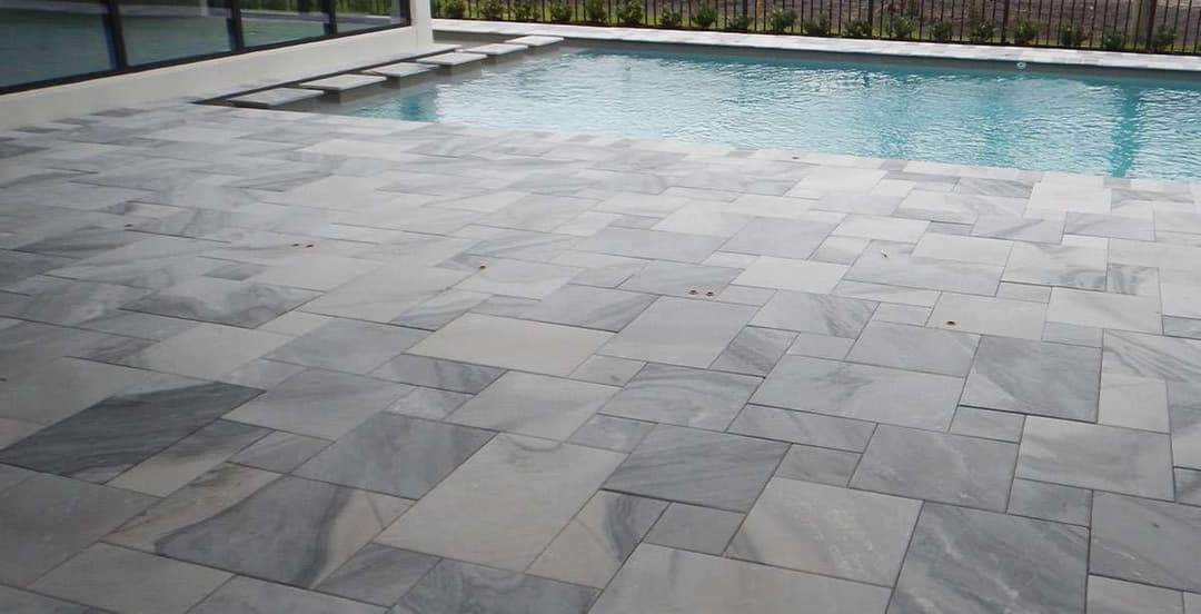 Modern gray marble pool deck with a clear blue swimming pool in a sunny outdoor setting.