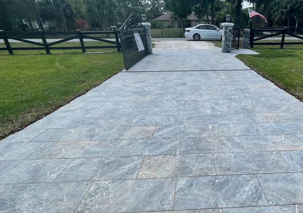 Newly paved driveway with gray stone tiles leading to a gated entrance and parked car.