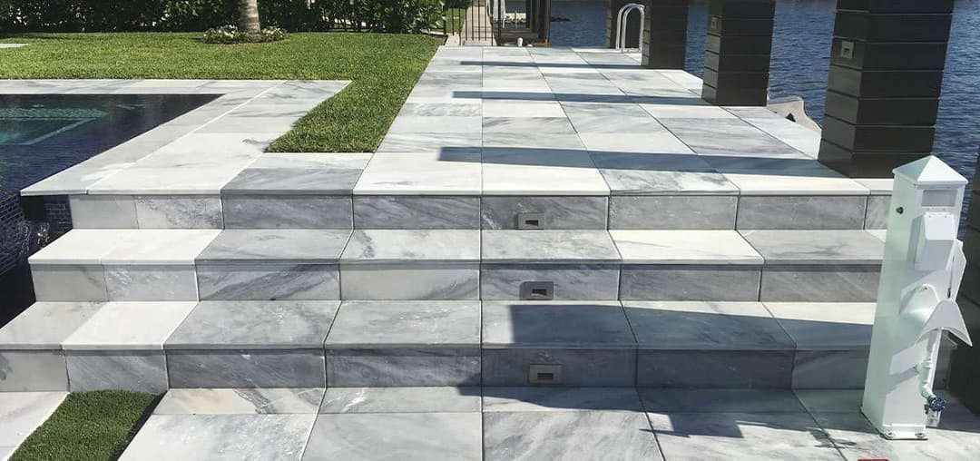 Marble terrace steps leading to a waterfront pool, showcasing elegant stone design.