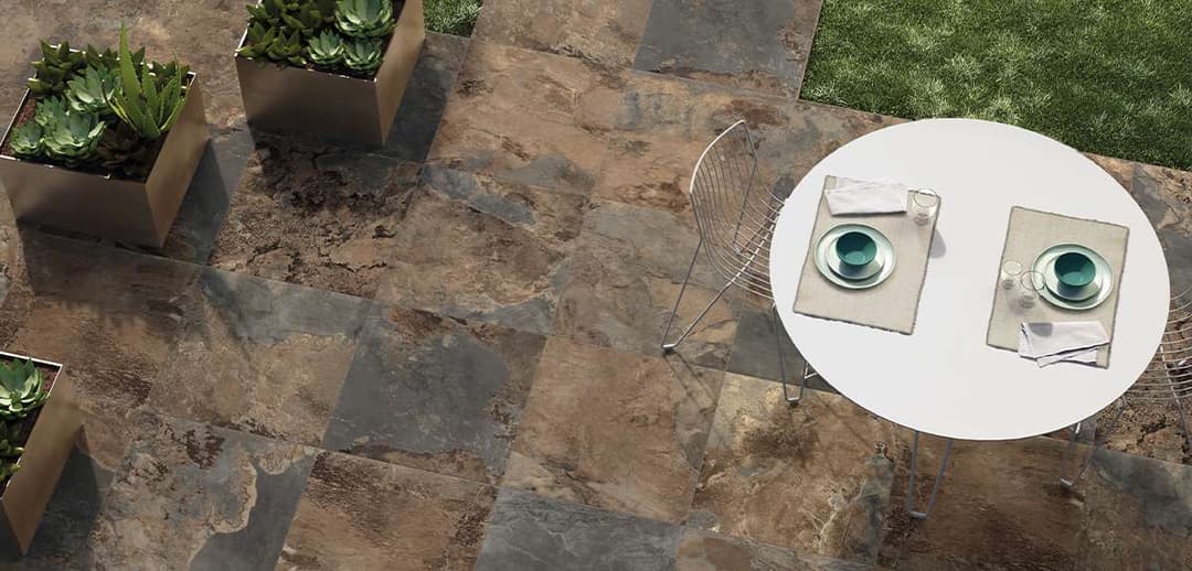 Outdoor dining area with a round table, teal dishware, and succulent plants on a stone patio.