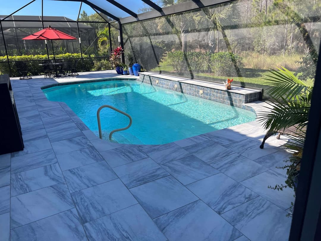 Luxury outdoor pool area with grey marble tiles, tropical plants, and a shaded seating area.
