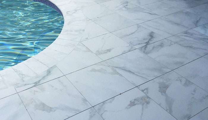 Marble pool deck surrounding clear water of a circular swimming pool.