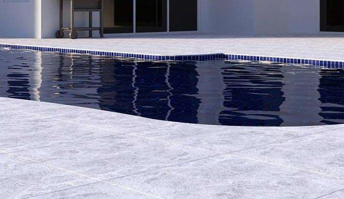 Modern swimming pool with blue tiles and sleek white patio area, reflecting sunlight.