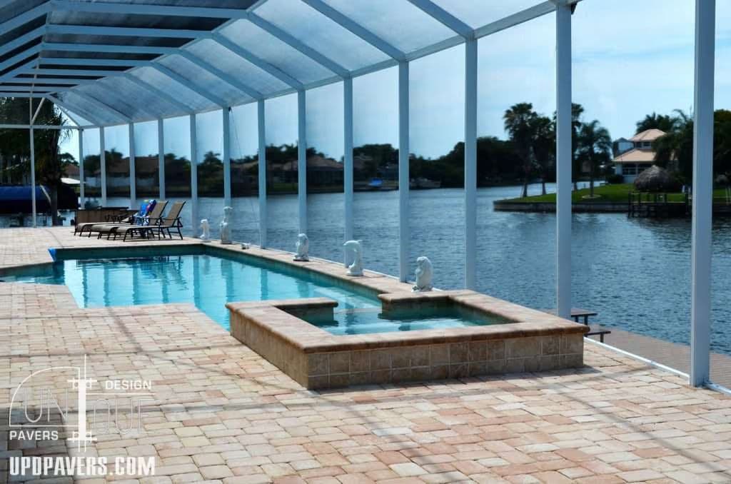 Luxury pool with spa and paver stones beside a serene lake and modern homes.