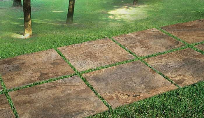 Paved pathway of brown stone tiles amidst green grass and trees.