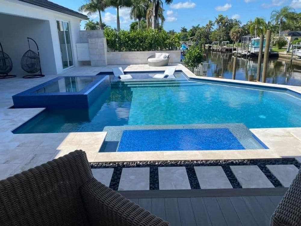 Luxury backyard pool with spa and water features, surrounded by palm trees and waterfront views.