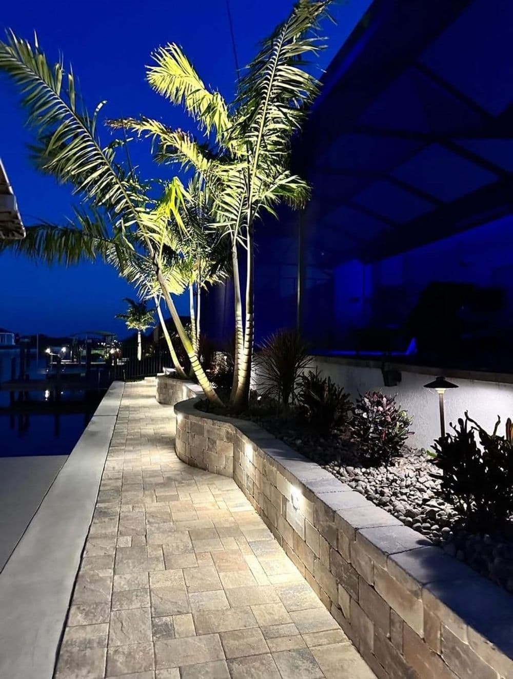 Illuminated pathway with palm trees and modern landscaping at night.